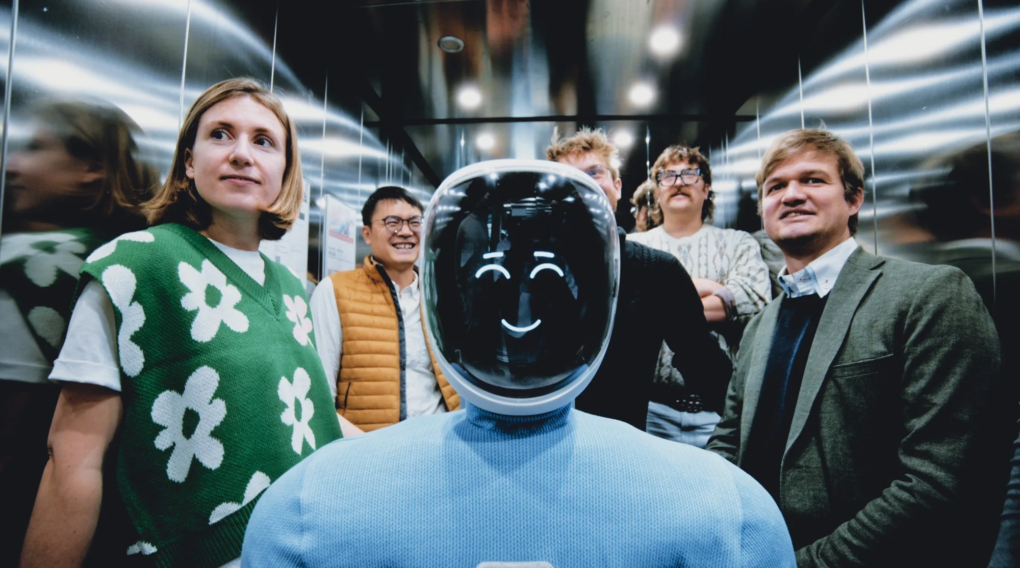 Plim smiling in a lift, surrounded by the Plim team.