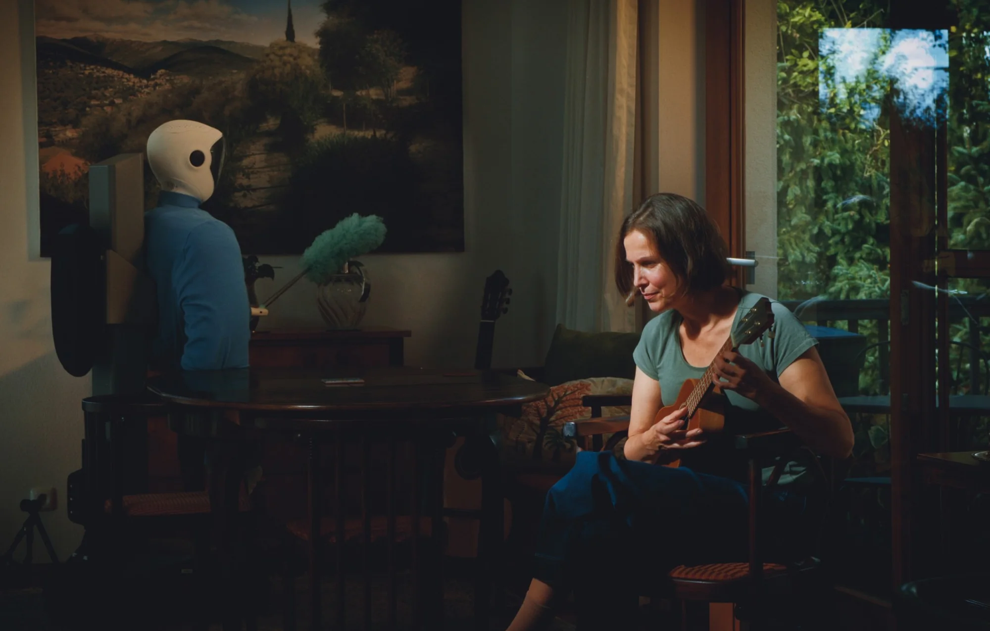Plim dusting in a living room while a woman plays the ukulele.