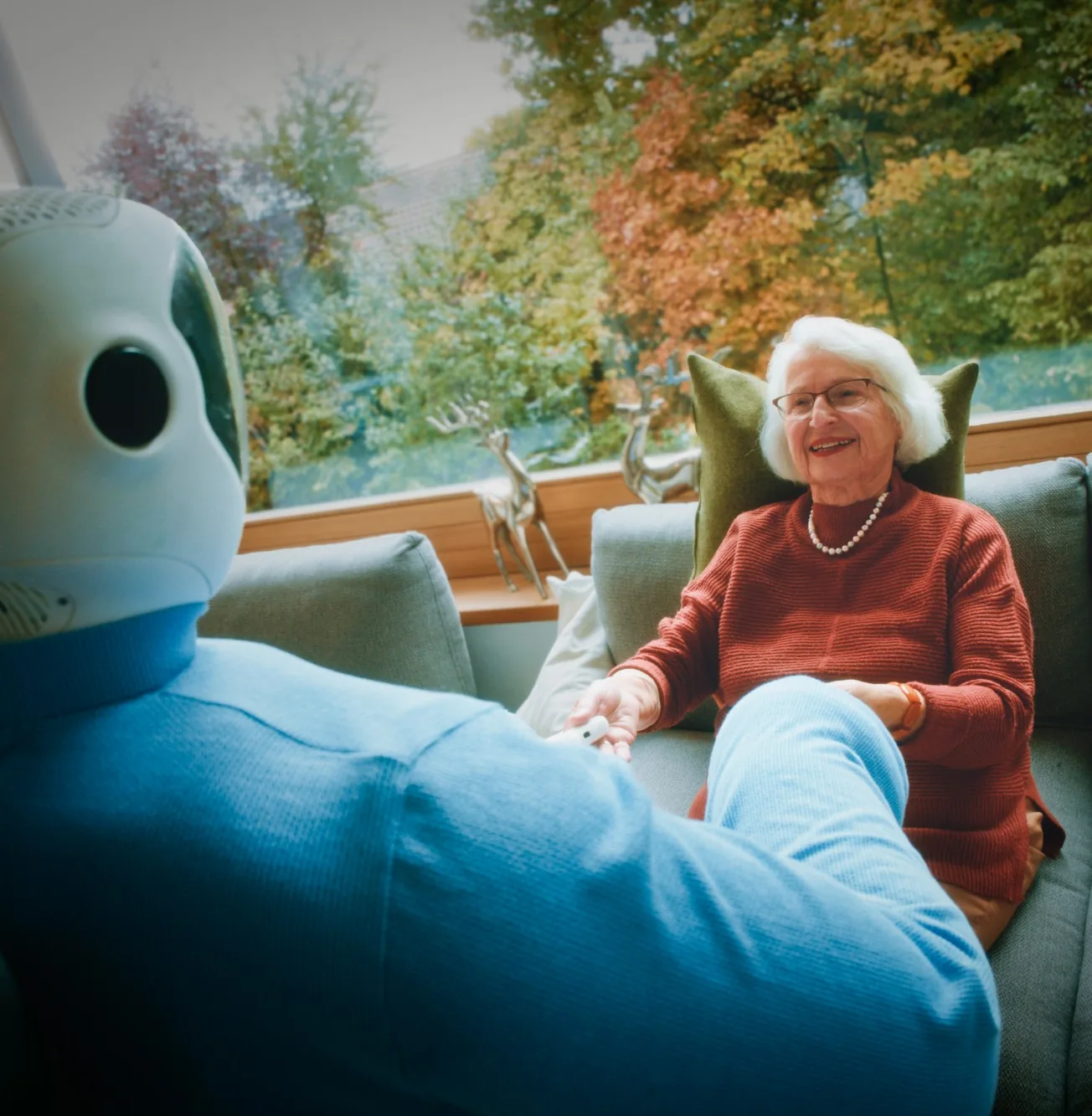An older woman laughing on her sofa while Plim holds her hand.